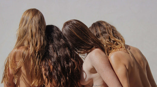 four women standing close together with their heads touching and their hair covering their skin