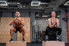 A shirtless, muscled man lifting a barbell with his left hand