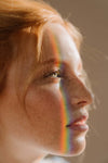 Side view of a bare-faced woman with a rainbow of light on her face