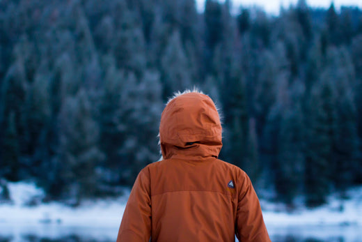 A woman wearing an orange jacket while outside during winter while looking at the trees.