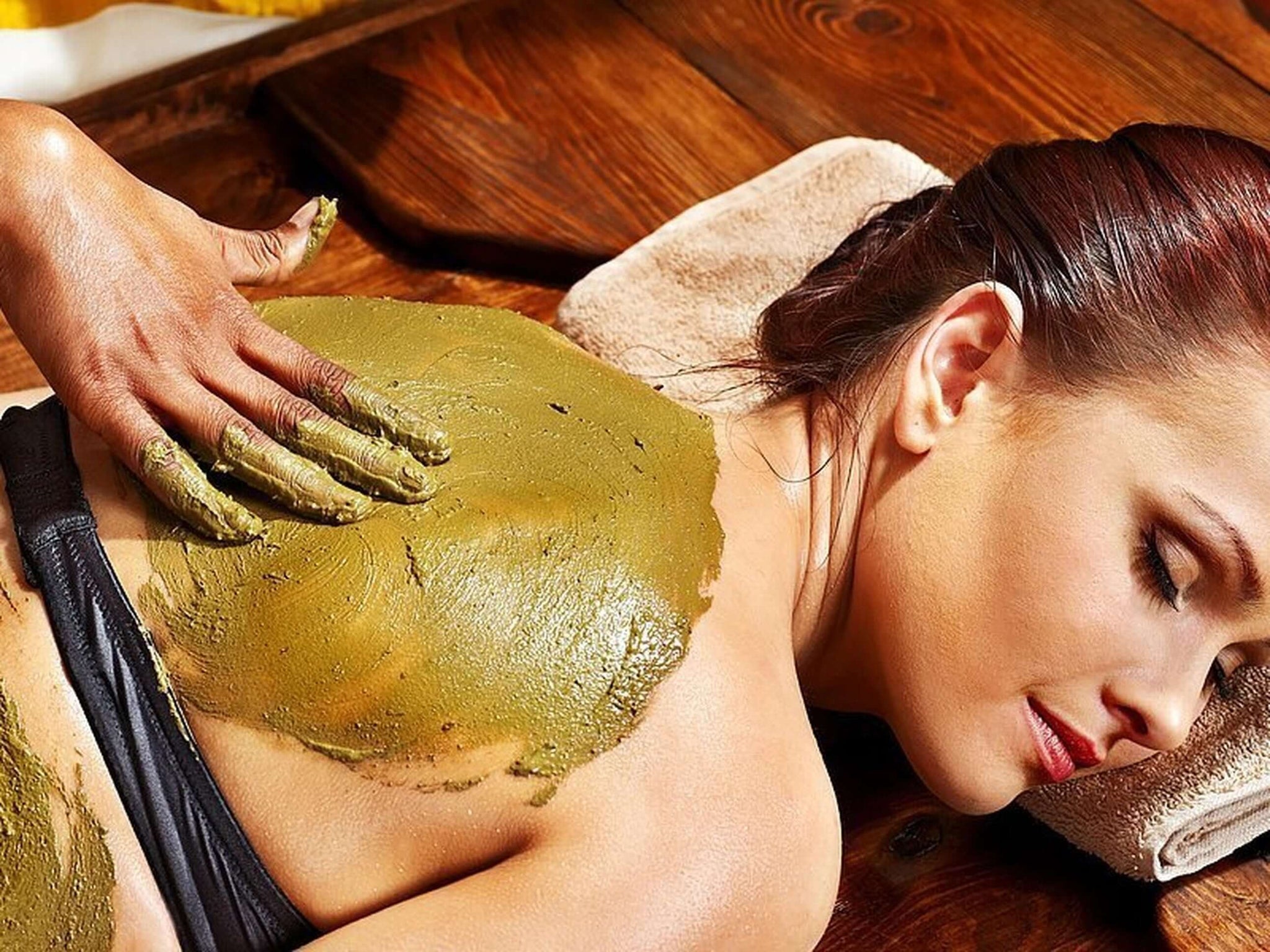 A woman lying down while being massaged with essential oils and clay.