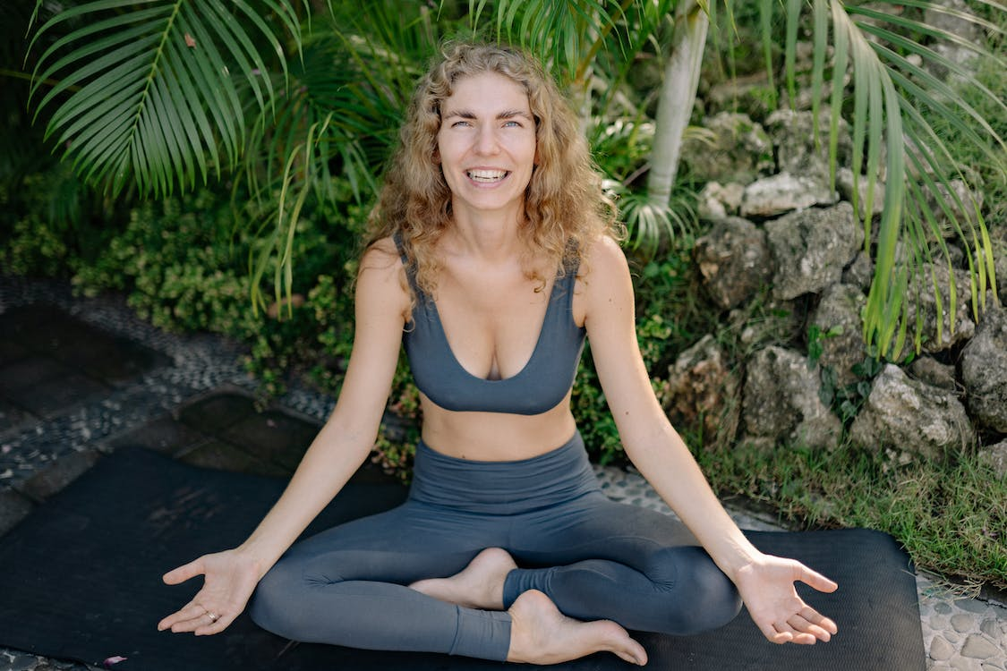 Woman smiling while doing yoga outdoors on a black mat
