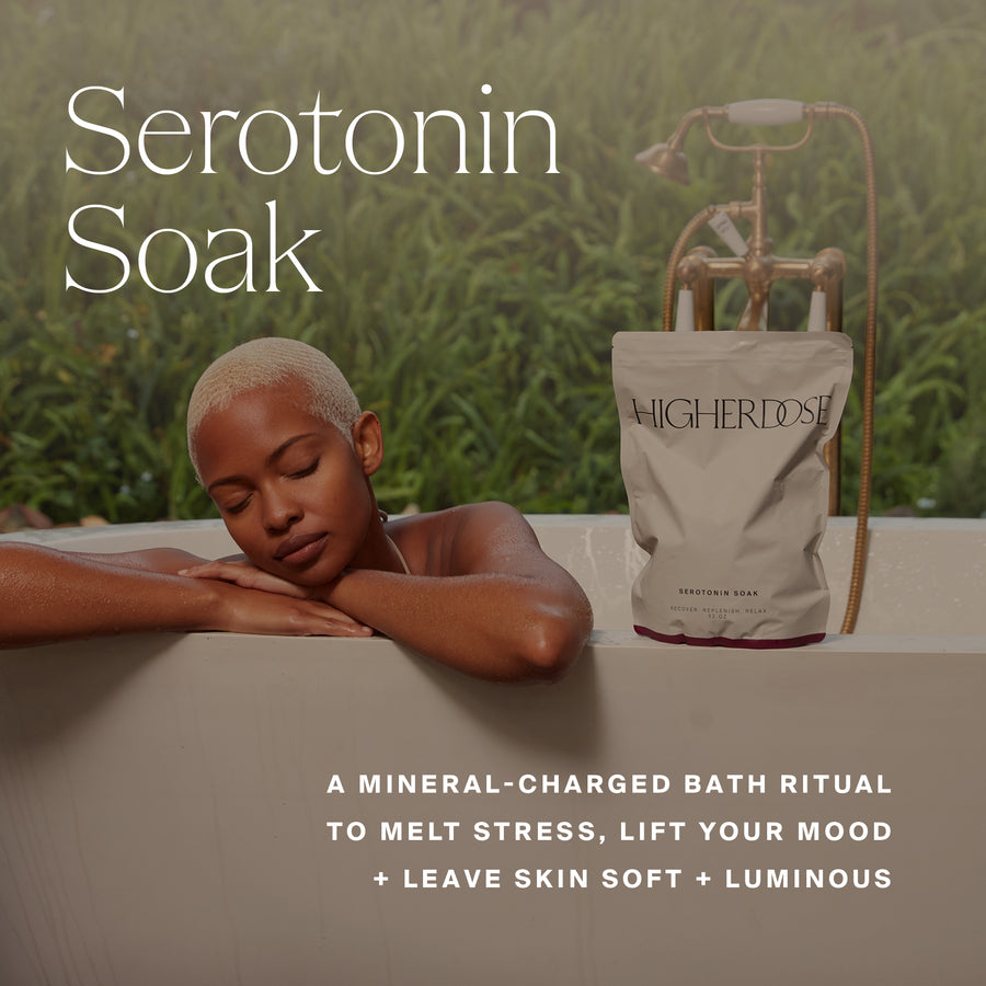 Person relaxing in bathtub next to Higher Dose Serotonin Soak bath salt package with vintage tub faucet and greenery backdrop