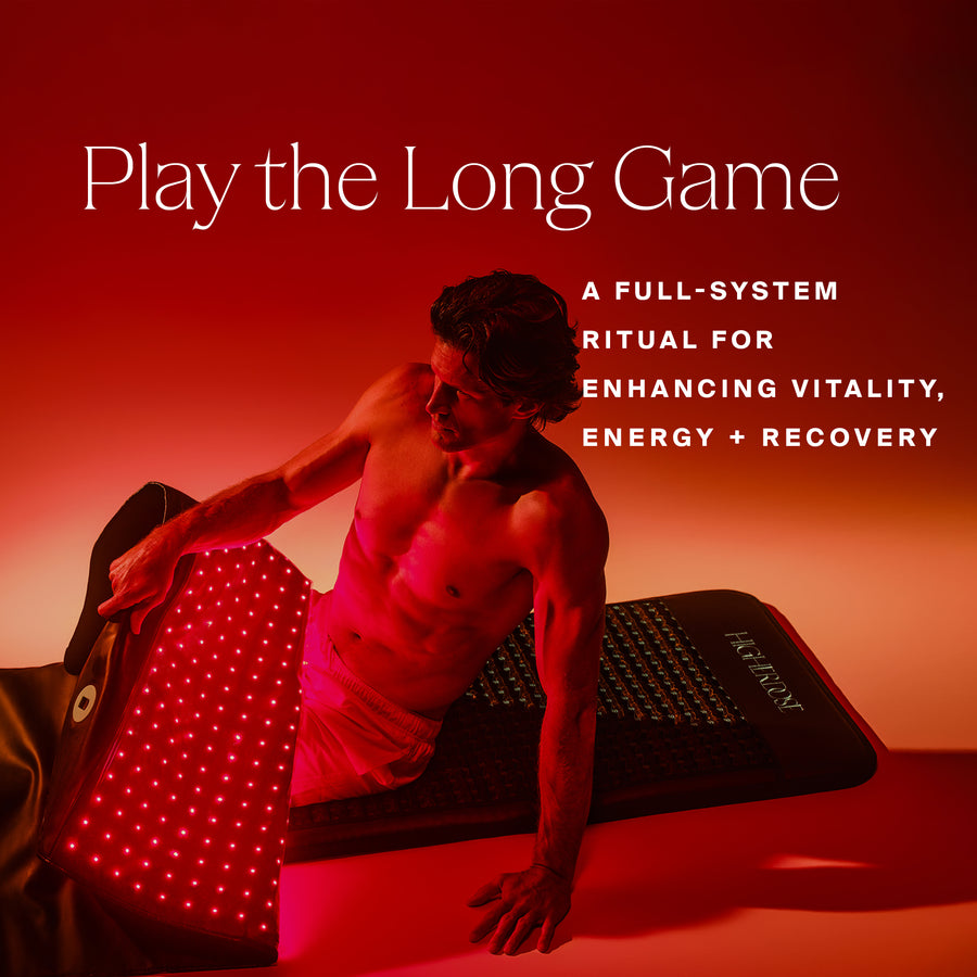 Shirtless man in plank position on red and black light therapy mats against warm red-orange background.