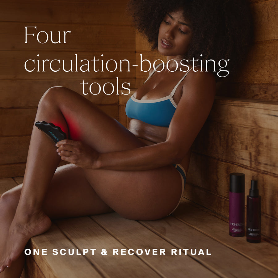 Woman in blue sports bra using handheld massage device on leg, with purple bottles displayed on wooden floor.