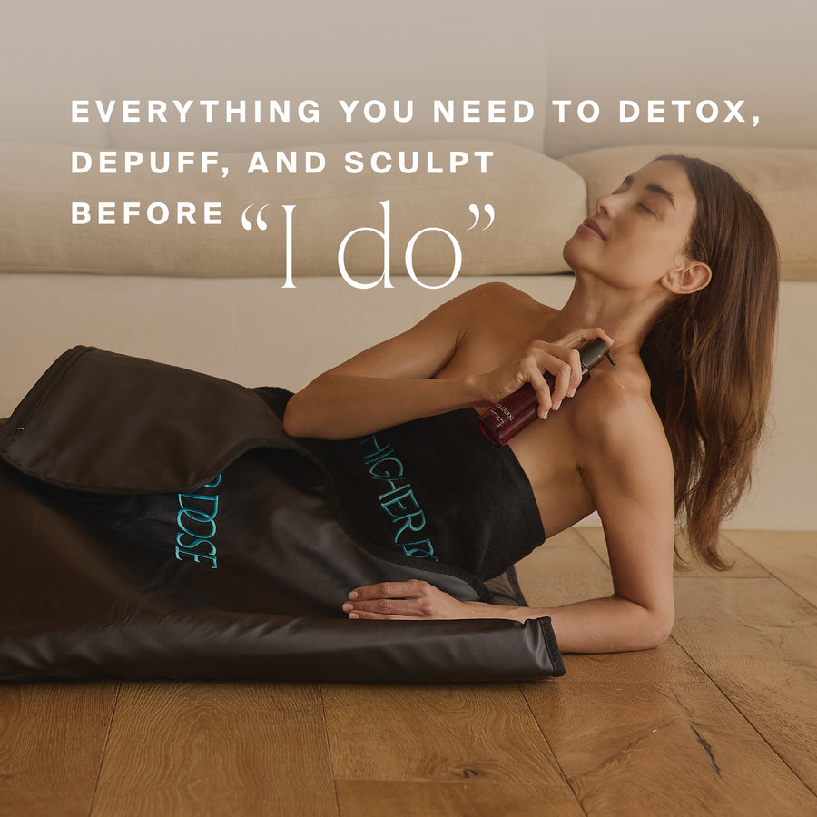 Woman sitting on wooden floor wearing black shorts with teal text, holding a dark bottle against her neck.