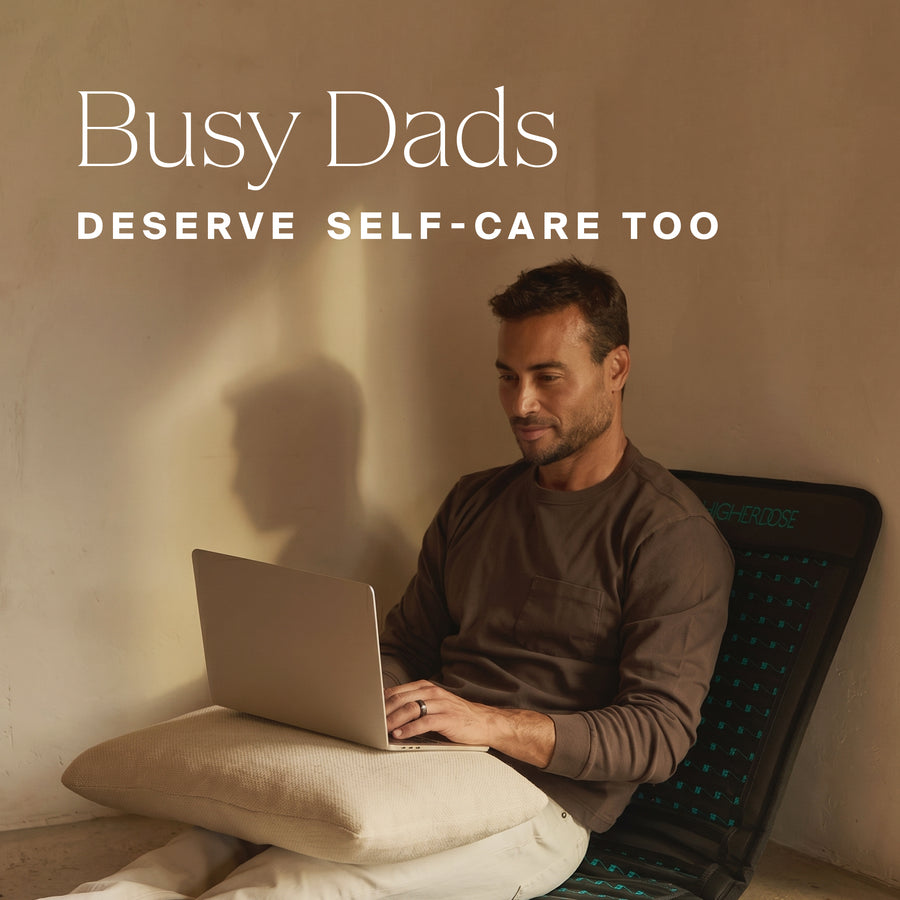 Man in brown shirt sitting on bed with laptop, leaning against pillow against tan wall.