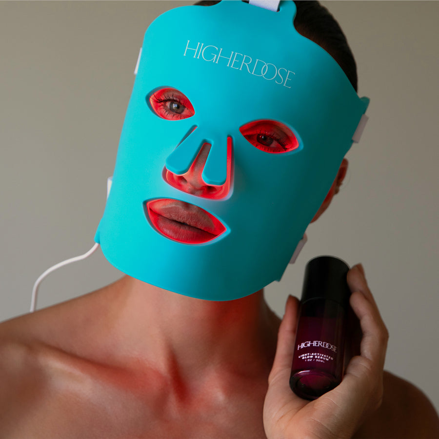 Turquoise LED face mask with red lip and eye cutouts displayed with dark purple serum bottle held in hand.