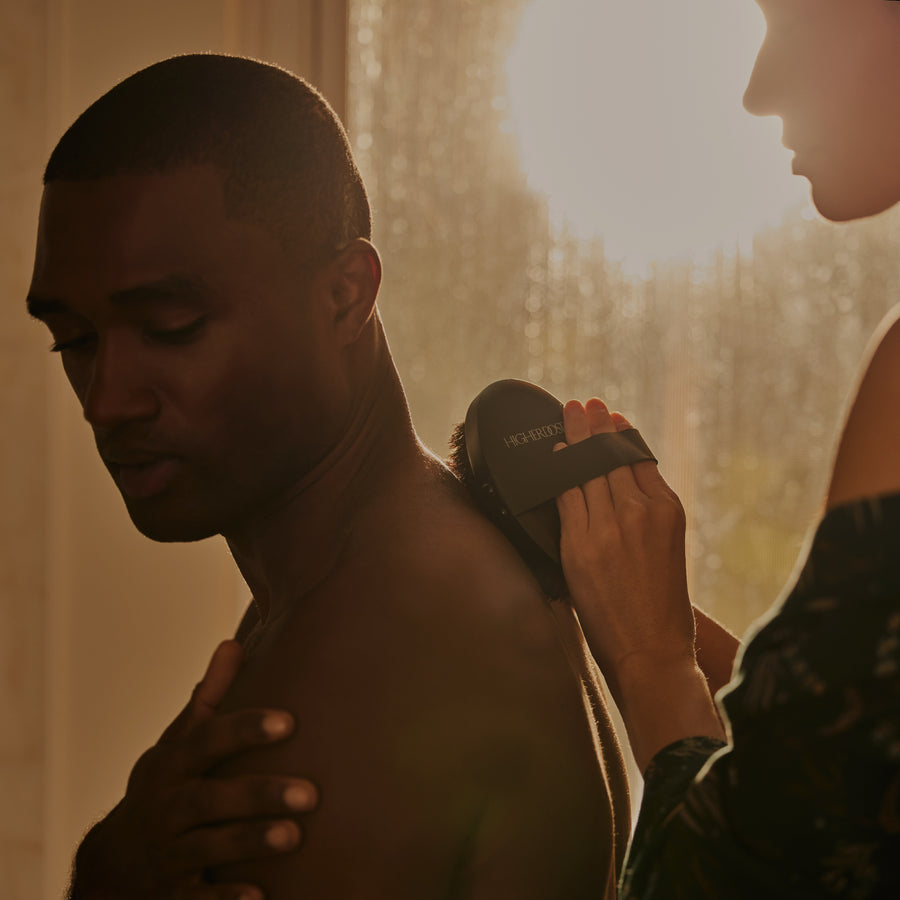 Person receiving shoulder massage with handheld massage device from another person indoors.