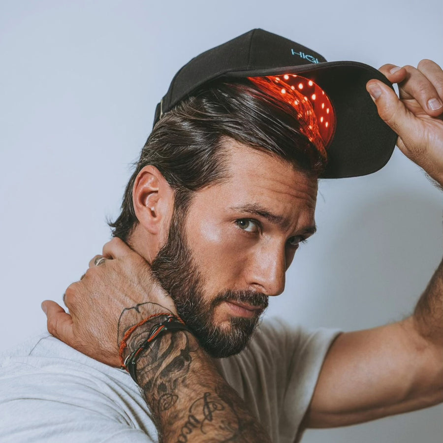 Man wearing black baseball cap with red patterned interior and light colored t-shirt against white background.