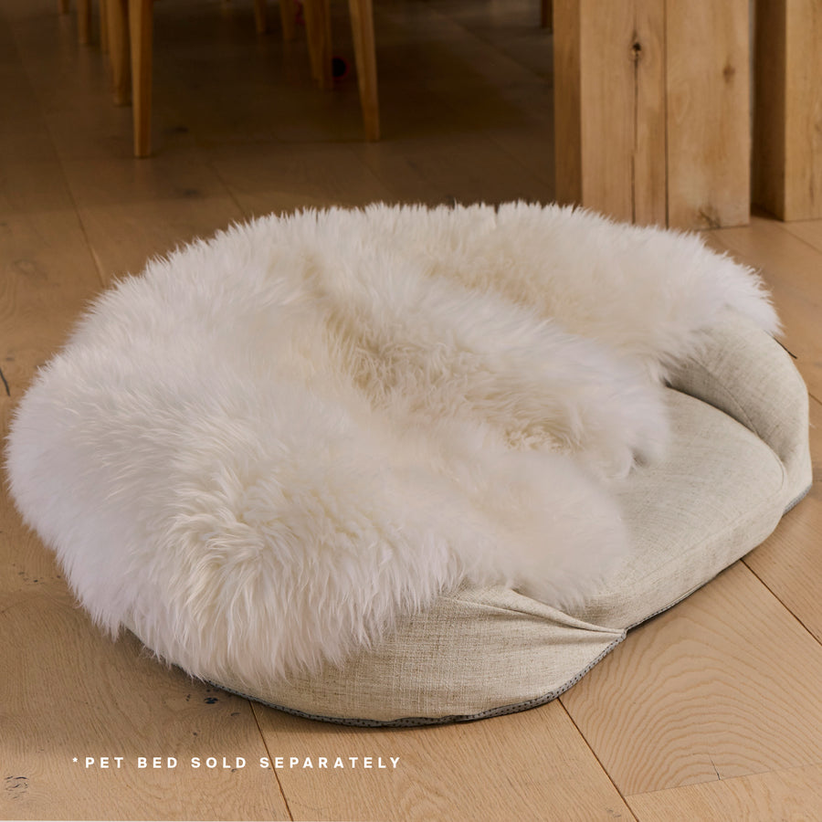 White shearling pet bed cover with fluffy wool top and beige fabric base on wooden floor.