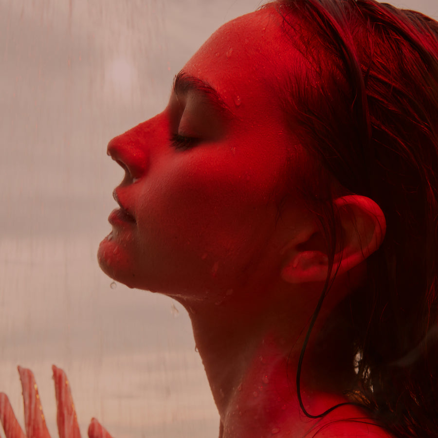Person's face and neck illuminated with red light during shower use.