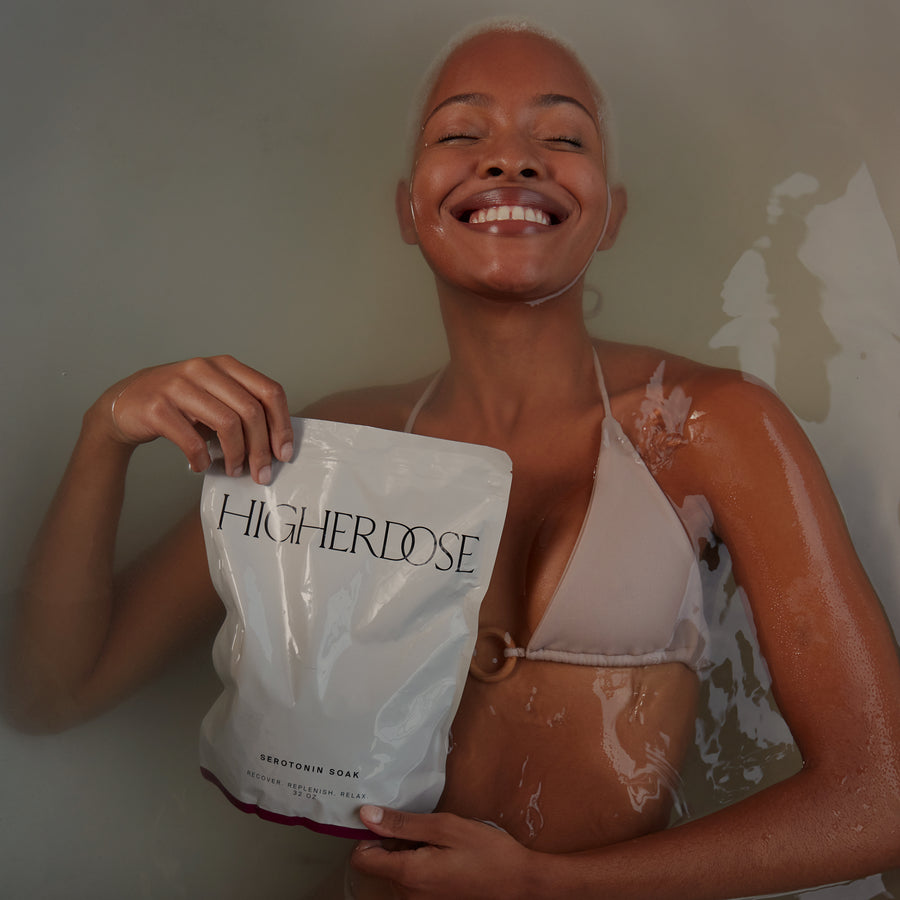 Woman holding Higher Dose Serotonin Soak product pouch while smiling with wet skin.