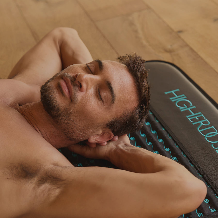 Man lying down with head resting on a dark recovery pillow with turquoise text and dotted pattern.