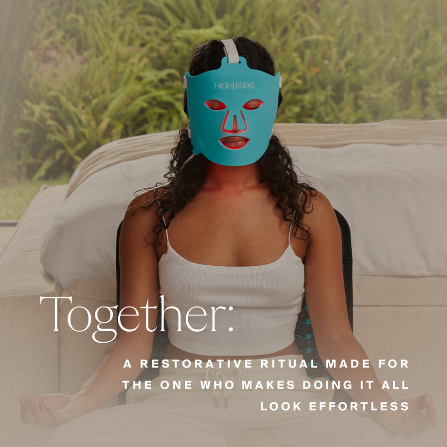 Person wearing turquoise LED light therapy face mask with red facial features on cream sofa.