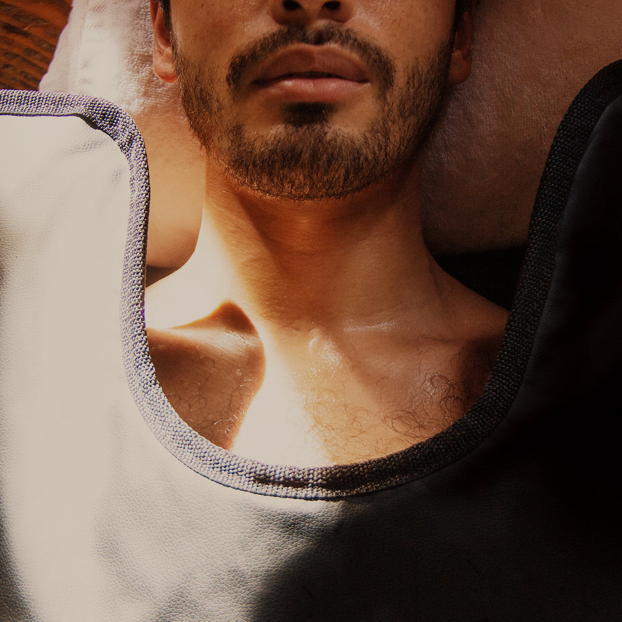 Man wearing white tank top with blue trim and black shirt against plain background.