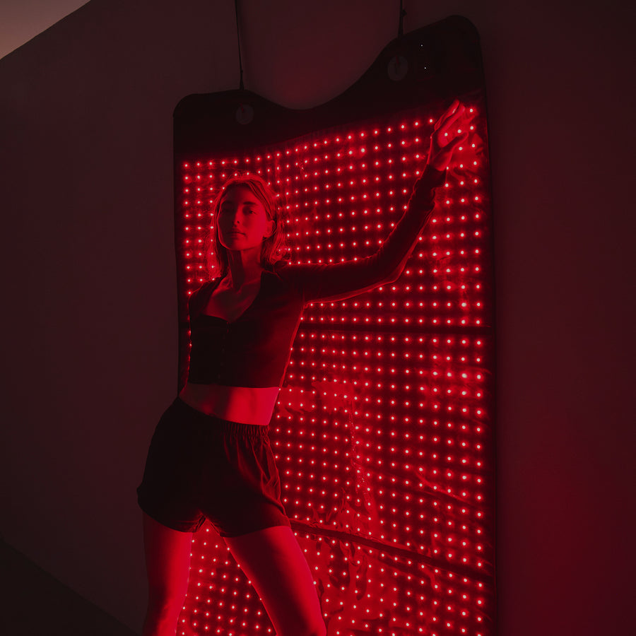 Person posing in front of a large wall-mounted red light panel with hundreds of LED lights.