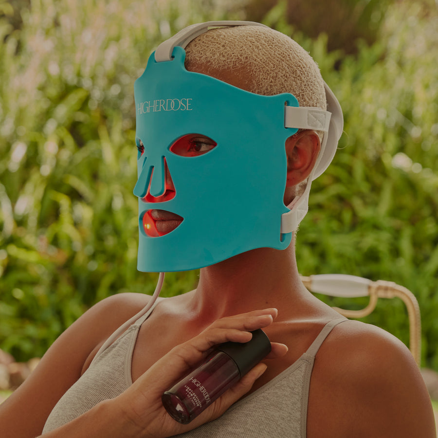 Turquoise silicone face mask with red cutout features worn by person holding dark bottle outdoors.
