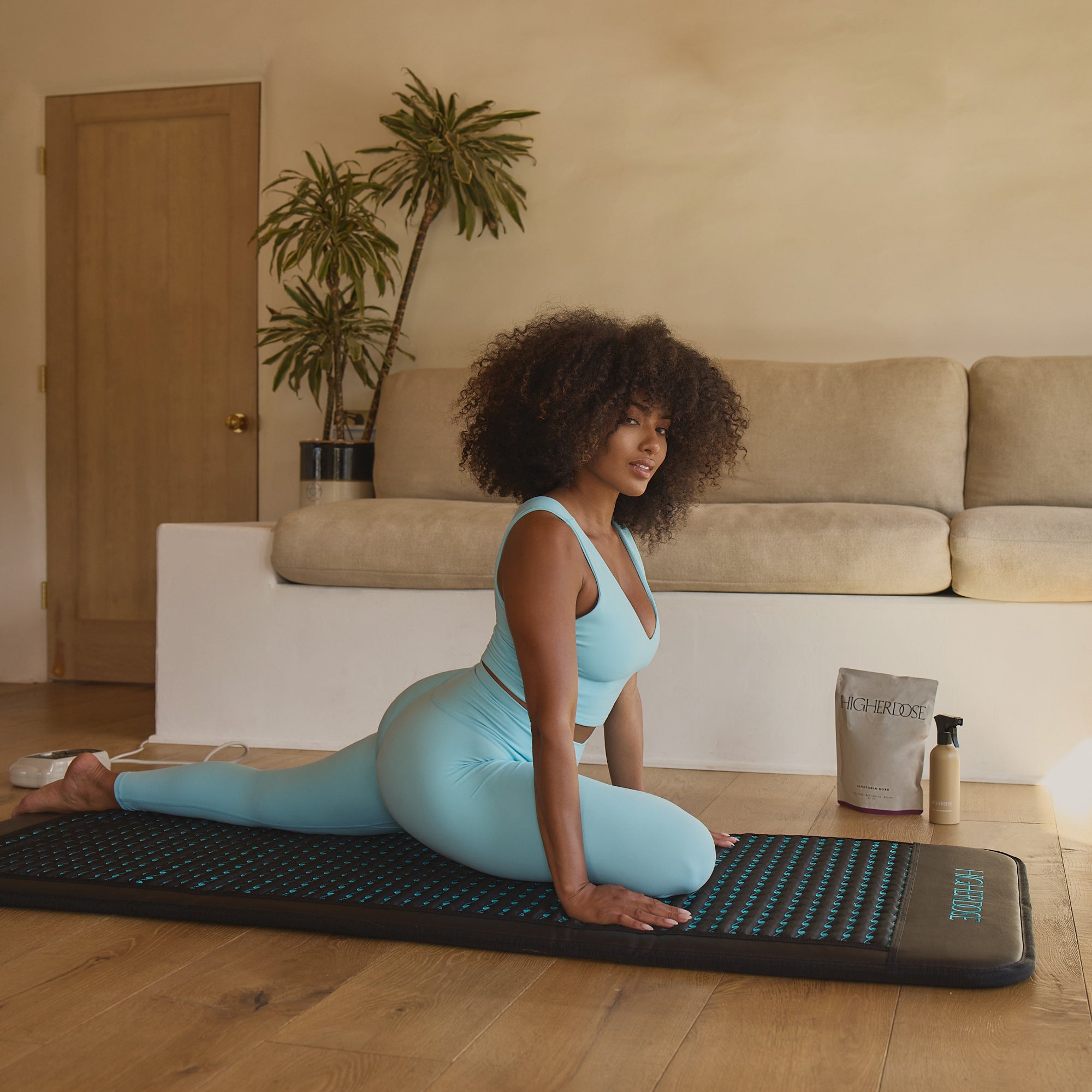 Woman in blue athletic wear practicing yoga on a mat in a living room.