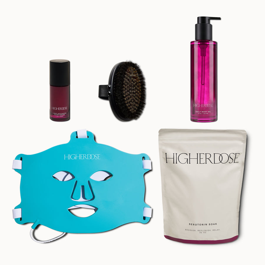Five-piece skincare set including burgundy serum, black facial brush, pink body oil, turquoise face mask, and white powder po