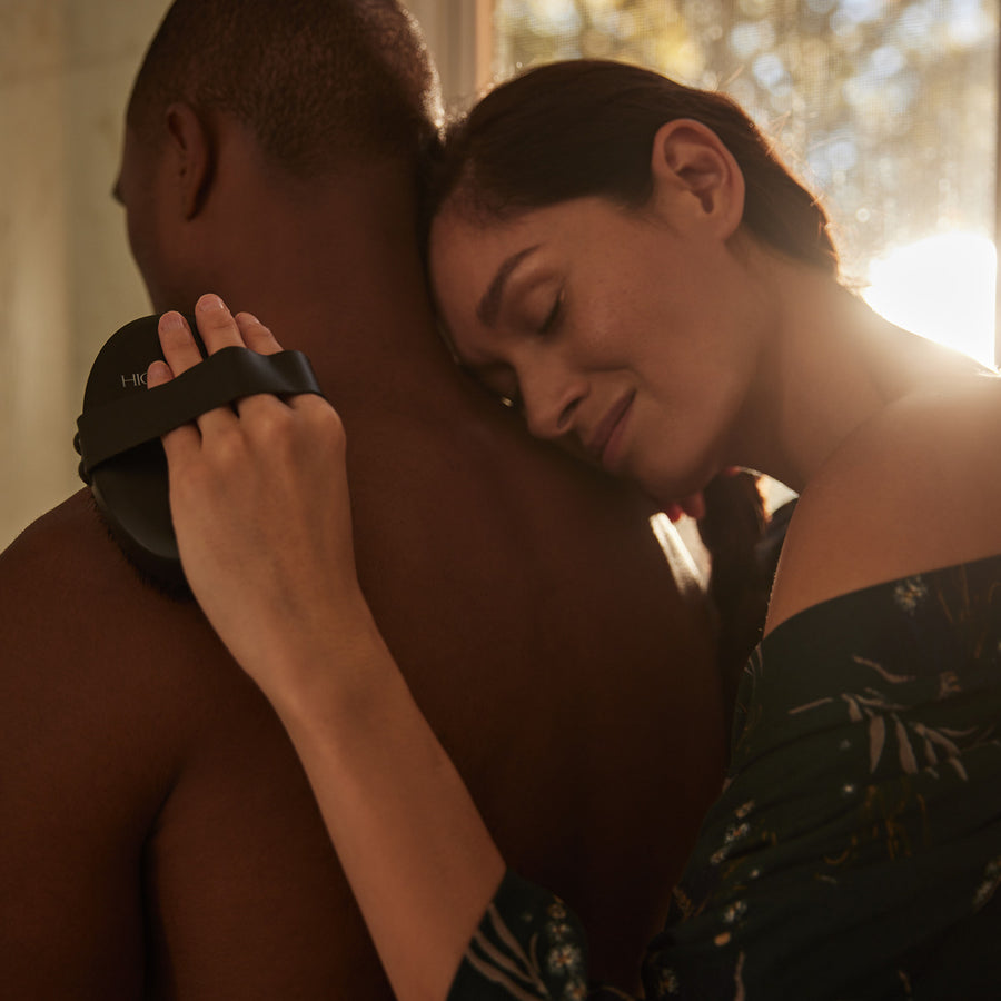 Woman holding black body brush with copper-colored band on man's shoulder.