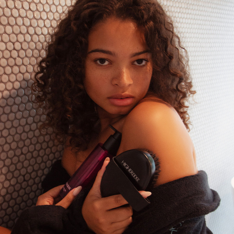 Person holding a black circular body brush with burgundy handle against shoulder.