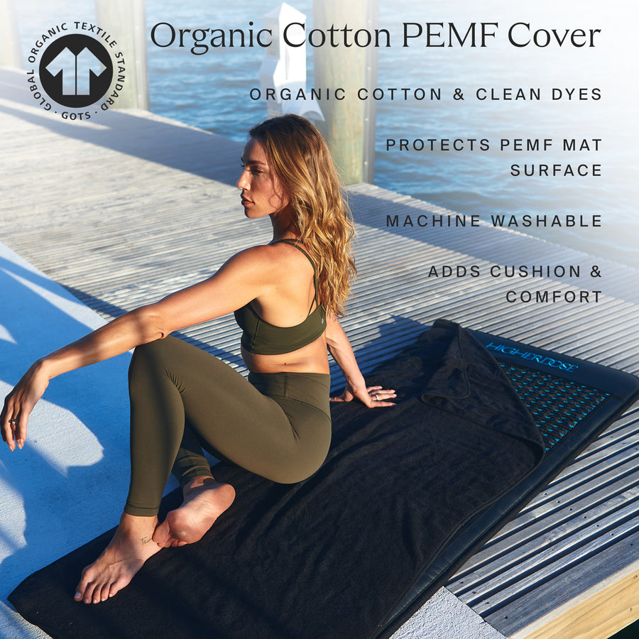 Woman sitting on black organic cotton PEMF mat cover with blue stripe pattern on waterfront deck.