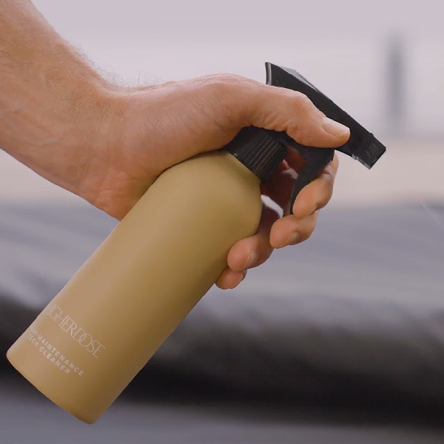 Hand holding tan spray bottle with black trigger pump against blurred background.