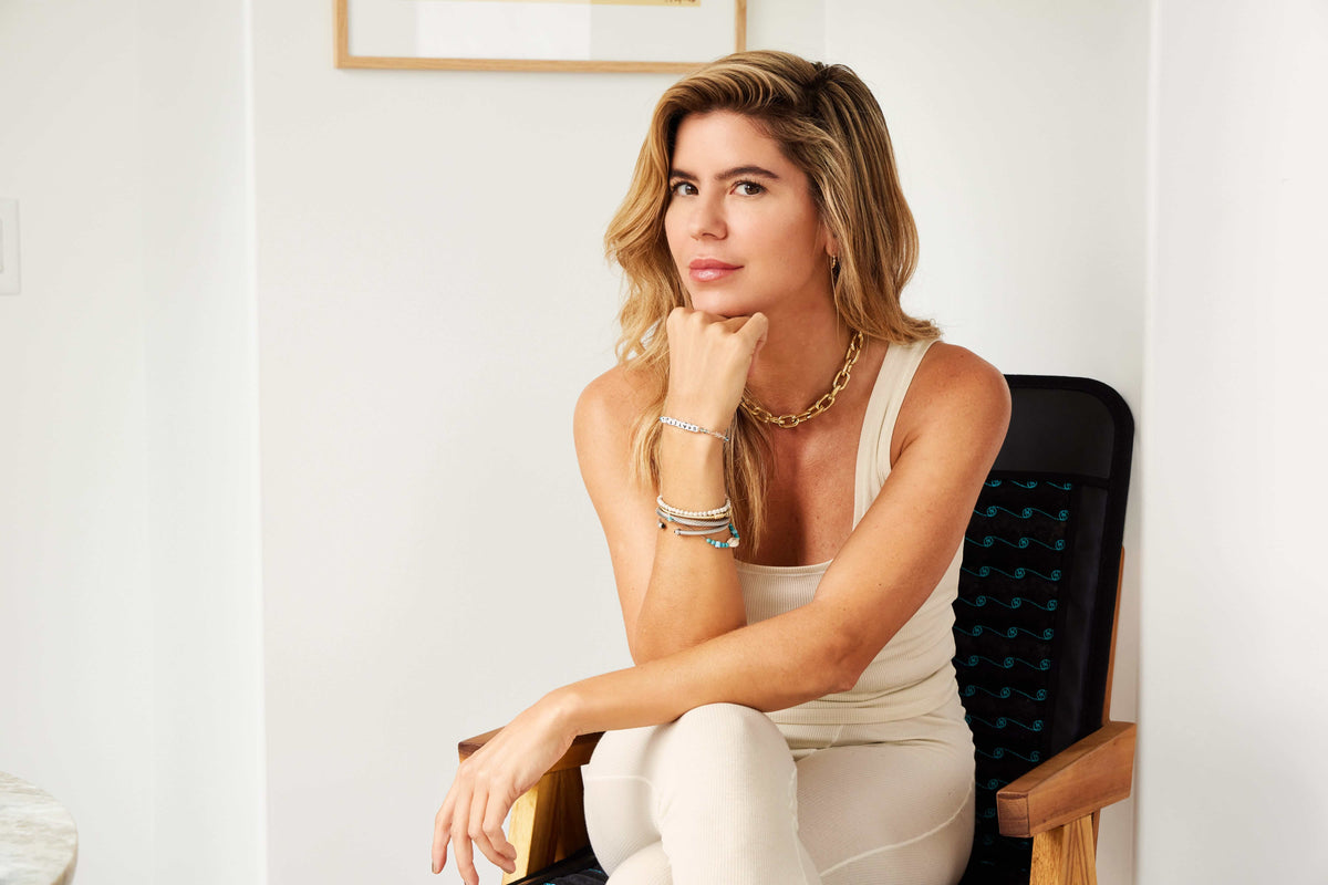HigherDOSE founder Katie Kaps seated indoors, resting her chin on her hand in a chair with a PEMF mat.