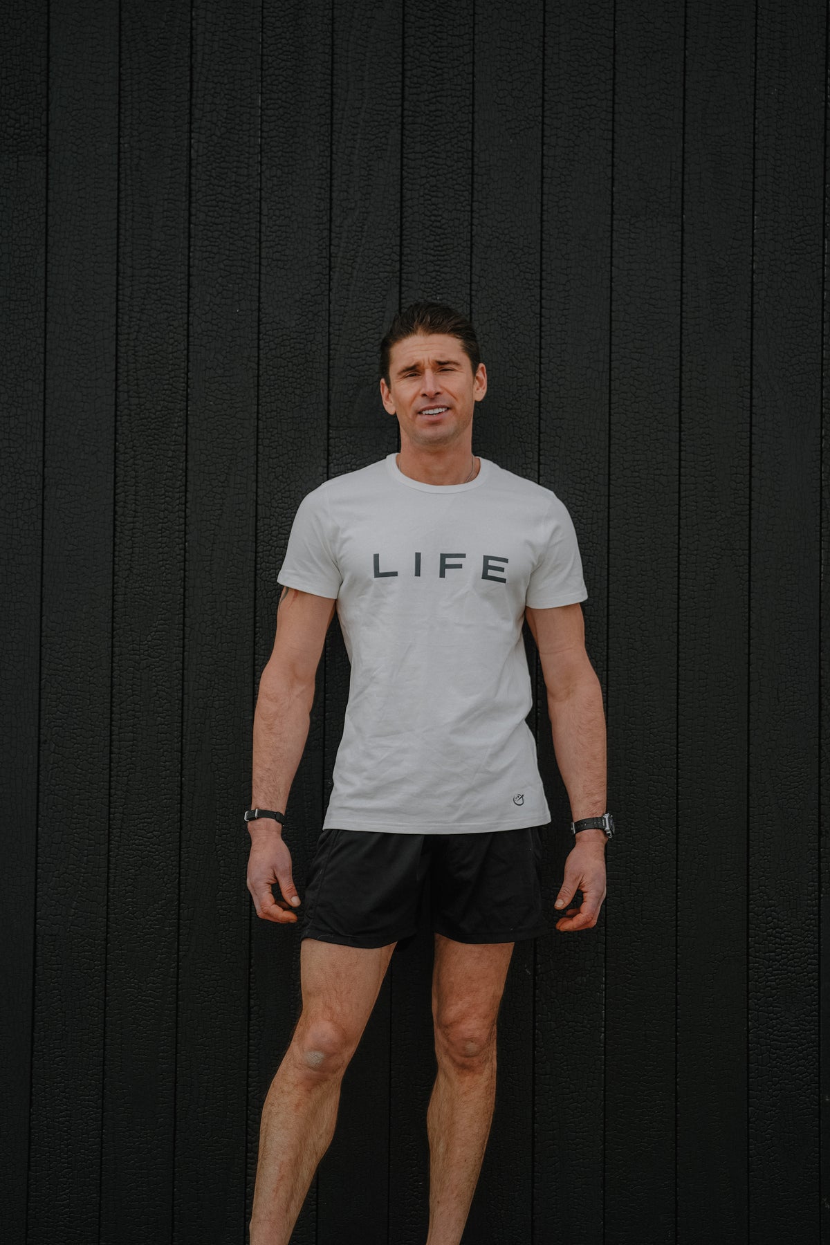 Man wearing a light gray t-shirt with 'LIFE' printed on it against a black background