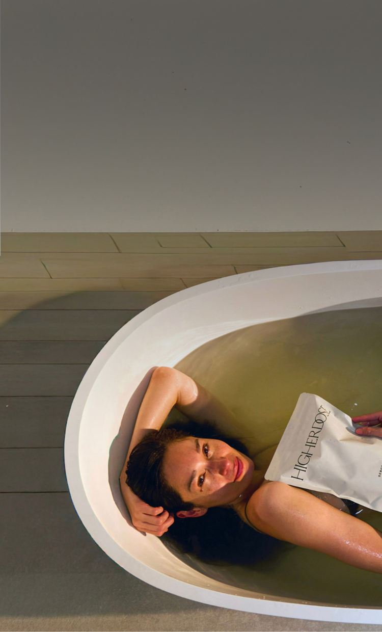 Woman lying in a bathtub with a magazine, surrounded by a neutral-toned room.
