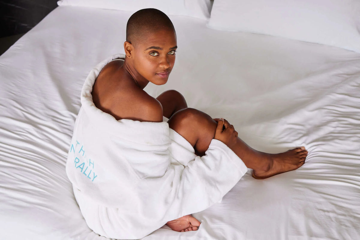 Person relaxing on a bed wearing the HigherDOSE 100% Organic Cotton Bath Robe, designed for post-sauna comfort and recovery.