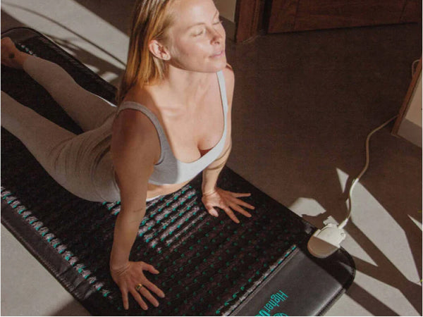 Woman stretching on a HigherDOSE PEMF mat in a yoga pose under warm light.