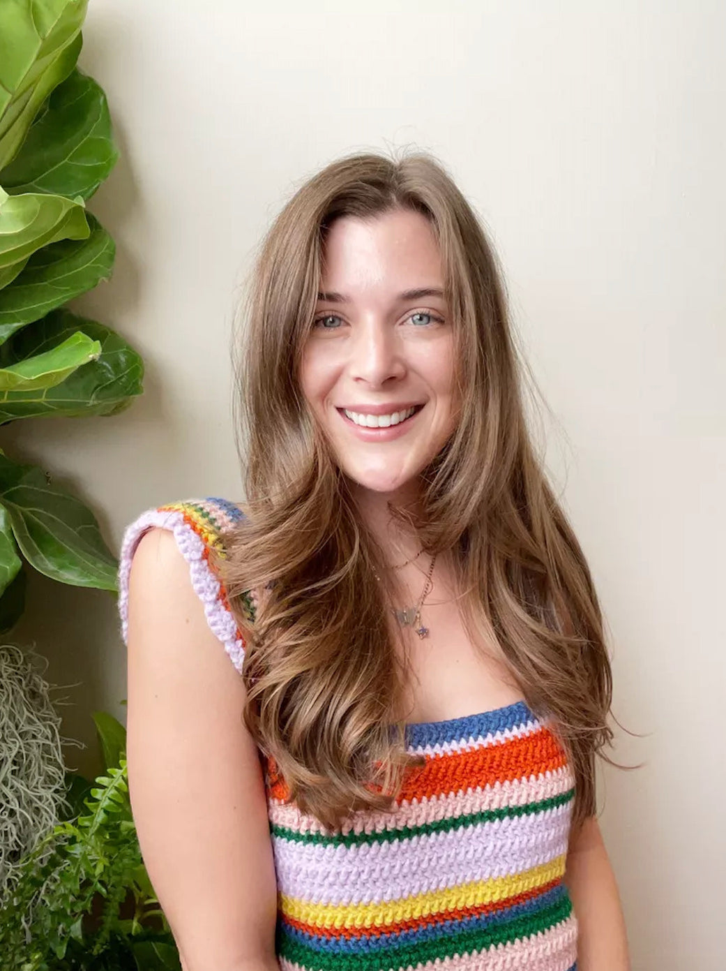 Woman smiling in a colorful striped knit top with plants in background.