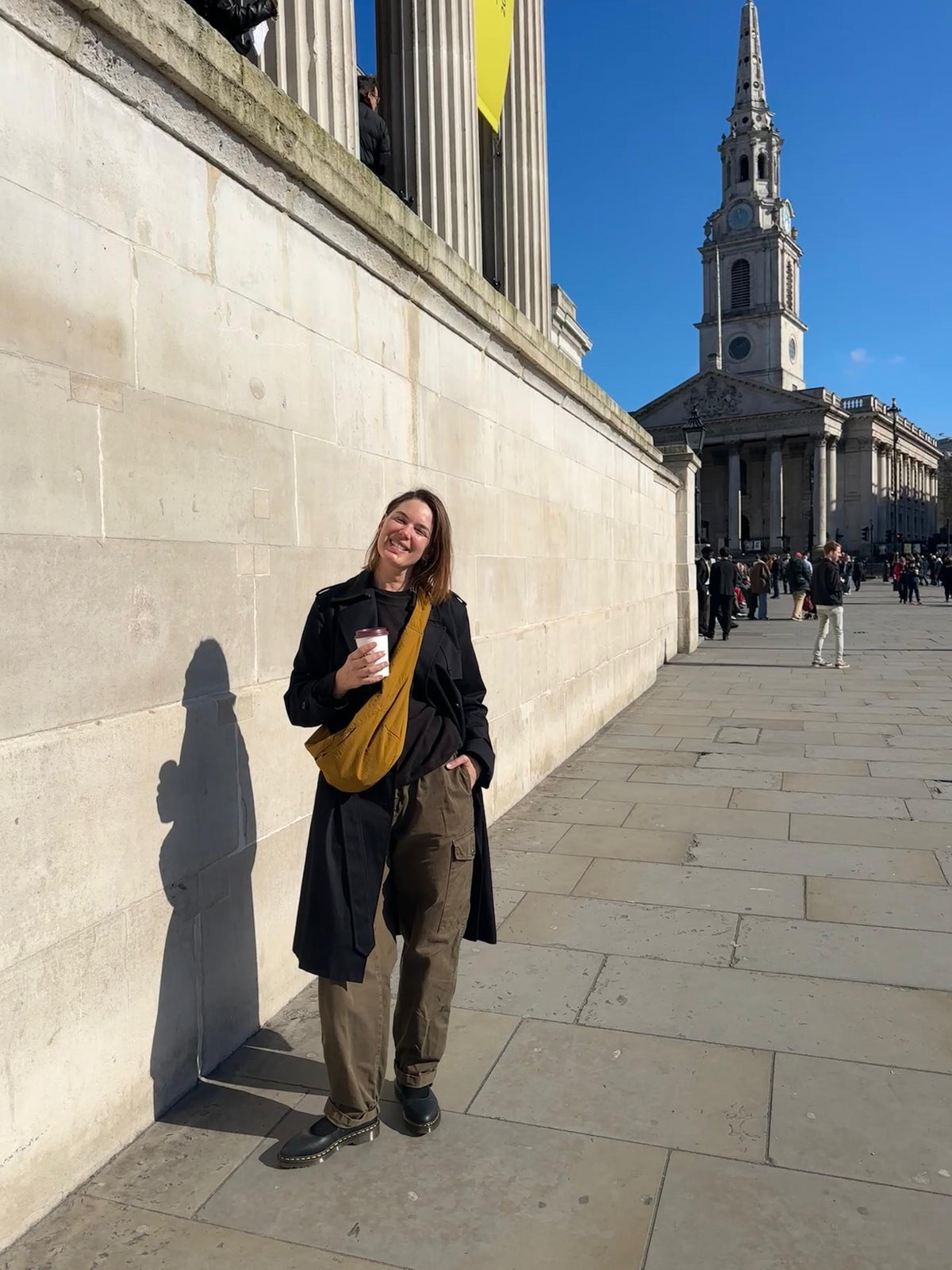 Woman standing outdoors against stone wall, holding a coffee cup.