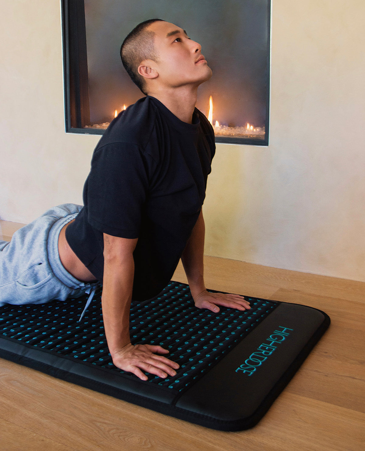 Person stretching on the HigherDOSE PEMF Mat in front of a fireplace, using electromagnetic therapy to relax and restore.