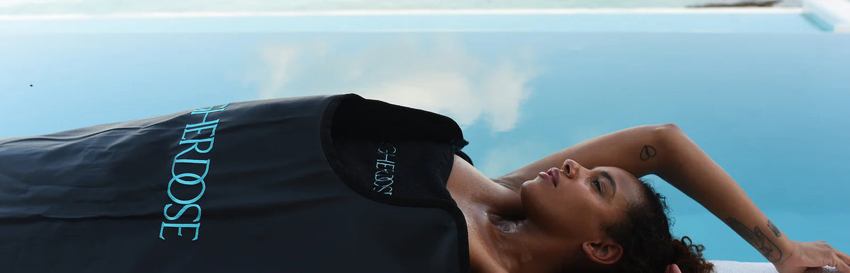 Person relaxing in the HigherDOSE Infrared Sauna Blanket by the water to promote detox, relaxation, and stress relief.