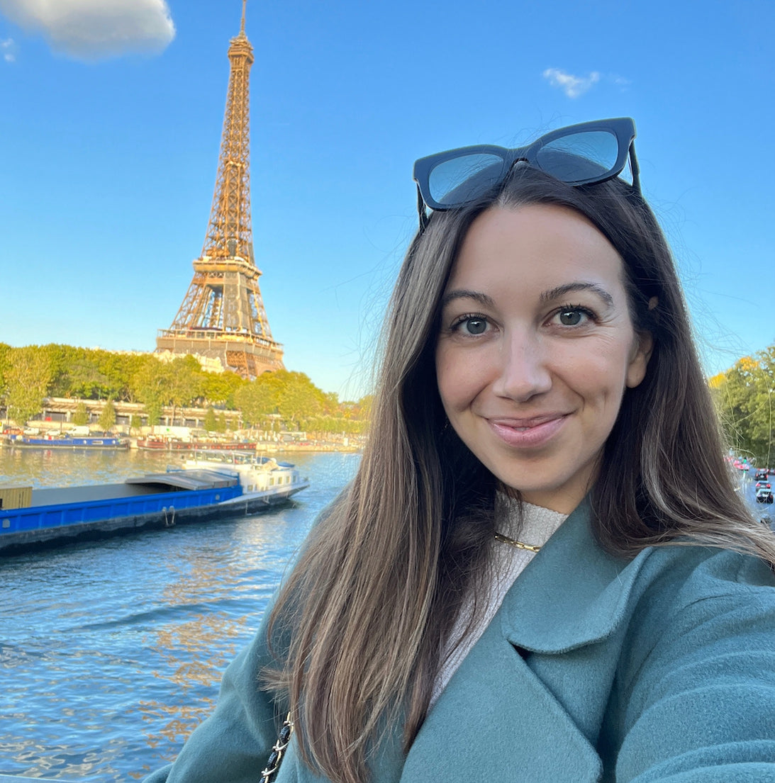 Woman smiling outdoors with the Eiffel Tower in the background on a sunny day.