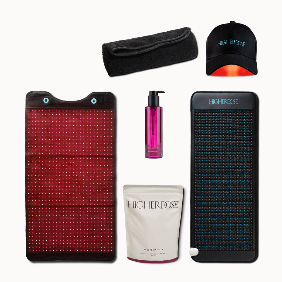 Skincare ritual set with red and blue light therapy panels, black headband cap, magenta liquid serum, white cream pouch, and 