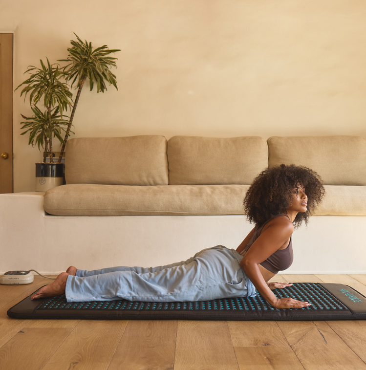 Woman exercising on a mat in a living room with a couch and plant in the background
