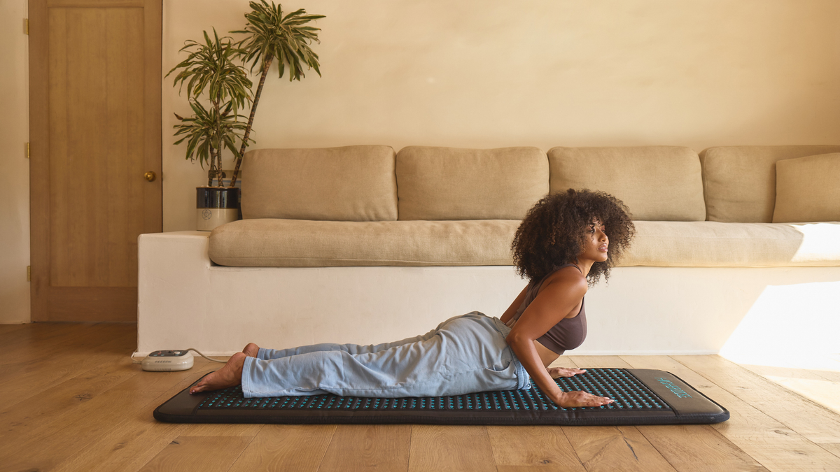 Woman exercising on a mat in a living room with a couch and plant in the background