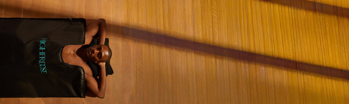 A man lies on a black mat on a wooden floor, wearing a black tank top
