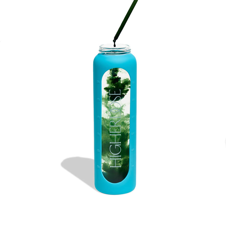 Tall glass water bottle with bright blue sleeve, clear cylindrical body containing turquoise liquid, and black straw inserted