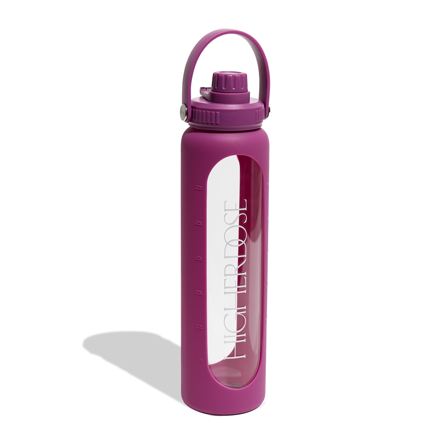 Purple water bottle with purple silicone sleeve, carry handle, screw-top lid, and time markers visible through clear glass ce