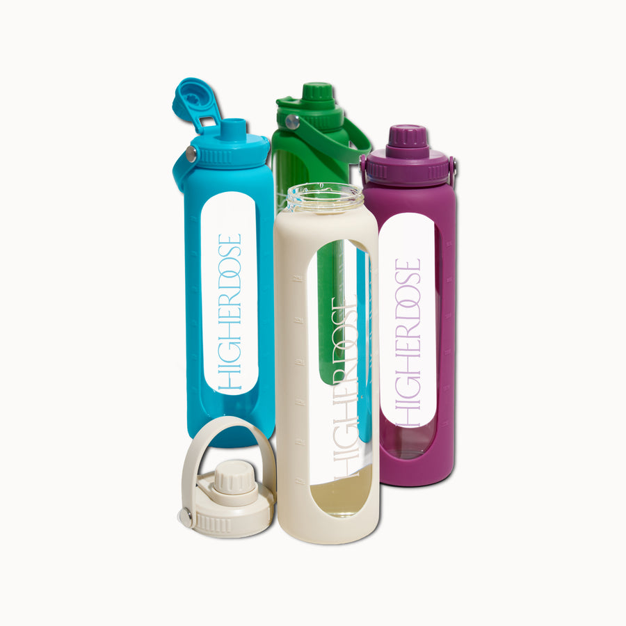 Three glass water bottles with flip-top caps in turquoise, cream, and purple, each with time markers and carrying handles.