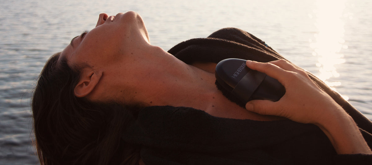 Woman by the water using the HigherDOSE Supercharge Copper Body Brush for a calming wellness ritual.