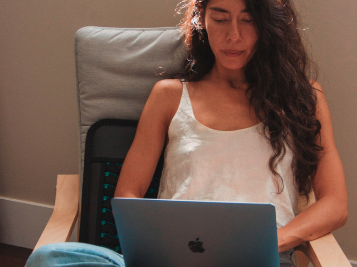 Woman working on a laptop while seated on a HigherDOSE PEMF mat.