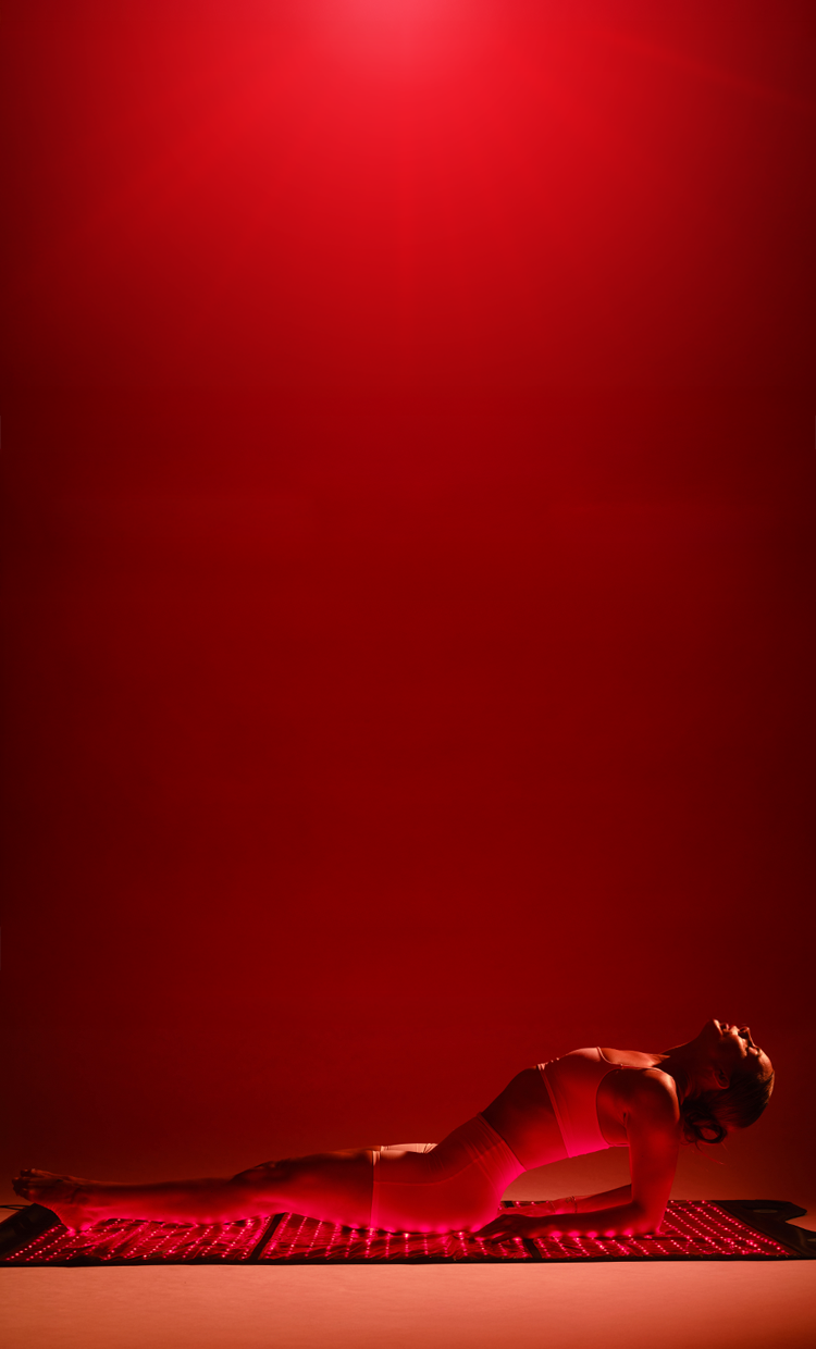 A person in a red-lit studio setting, lying on a textured mat against a solid red background.